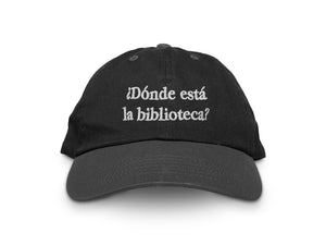 Image of front of black hat with "¿Dóndé está lá biblioteca?" embroidered in white