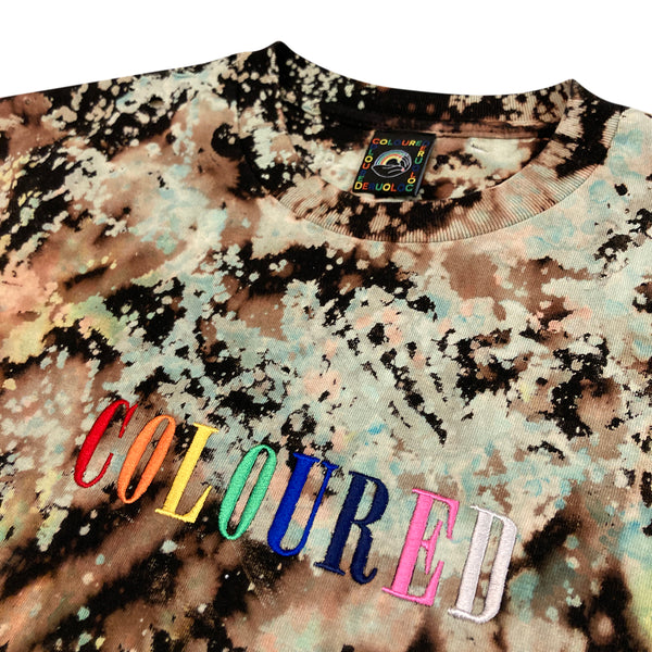 An image of a black t-shirt with green and beige splatters and "COLOURED" embroidered in rainbow colors.