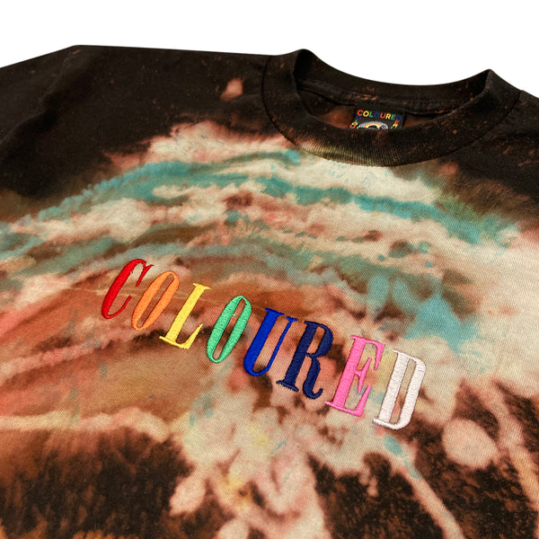 An image of a black t-shirt with the Coloured Publishing logo bleached and dyed on, with "COLOURED" written on the bottom and "COLOURED" embroidered in rainbow colors.
