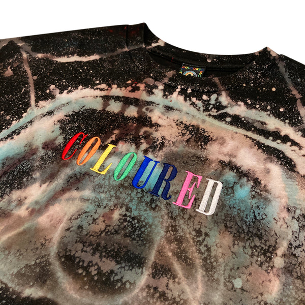 An image of a black t-shirt with bleached and dyed face with afro and "COLOURED" embroidered in rainbow colors.