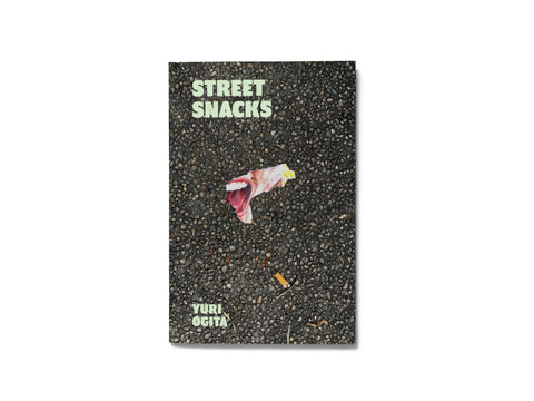 Image of the front cover of the book "Street Snacks," depicting a torn picture of a mouth on a street between the text "Street Snacks" and "Yuri Ogita."