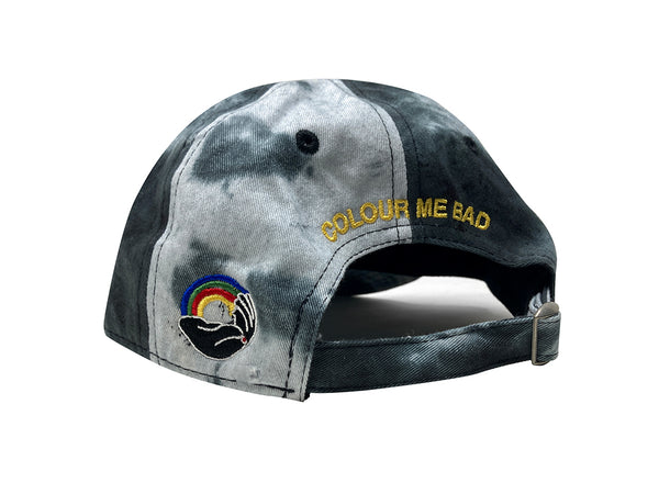 An image of the three-quarters view of a black and white tie-dyed hat with "COLOUR ME BAD" embroidered in yellow and the Coloured Publishing logo embroidered in full color on the side..