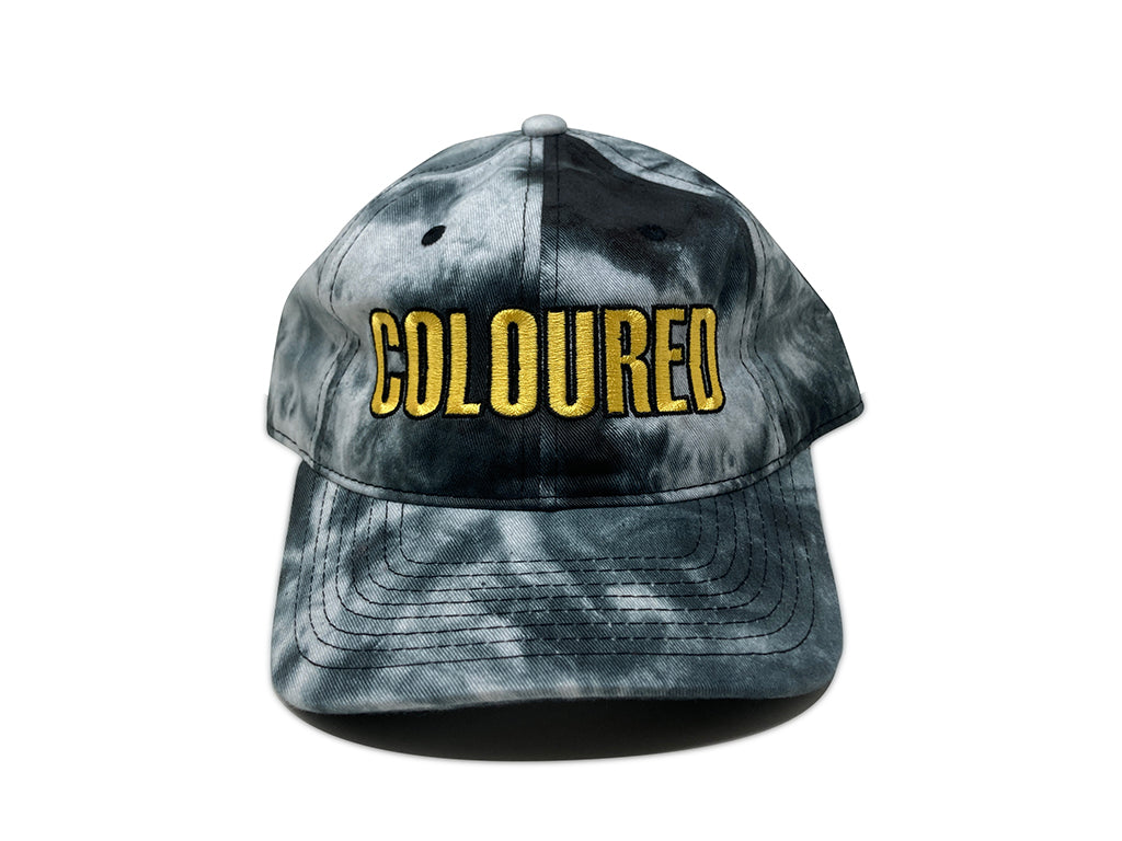 An image of the front of a black and white tie-dyed hat with "COLOURED" embroidered in yellow and black.