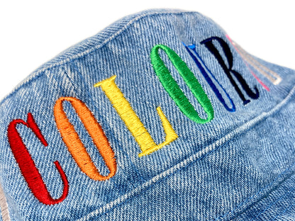 Image of a light denim bucket hat with "COLOURED" embroidered in rainbow letters.