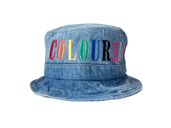 Image of a light denim bucket hat with "COLOURED" embroidered in rainbow letters.