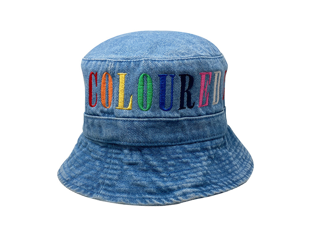 Image of a light denim bucket hat with "COLOURED" embroidered in rainbow letters.